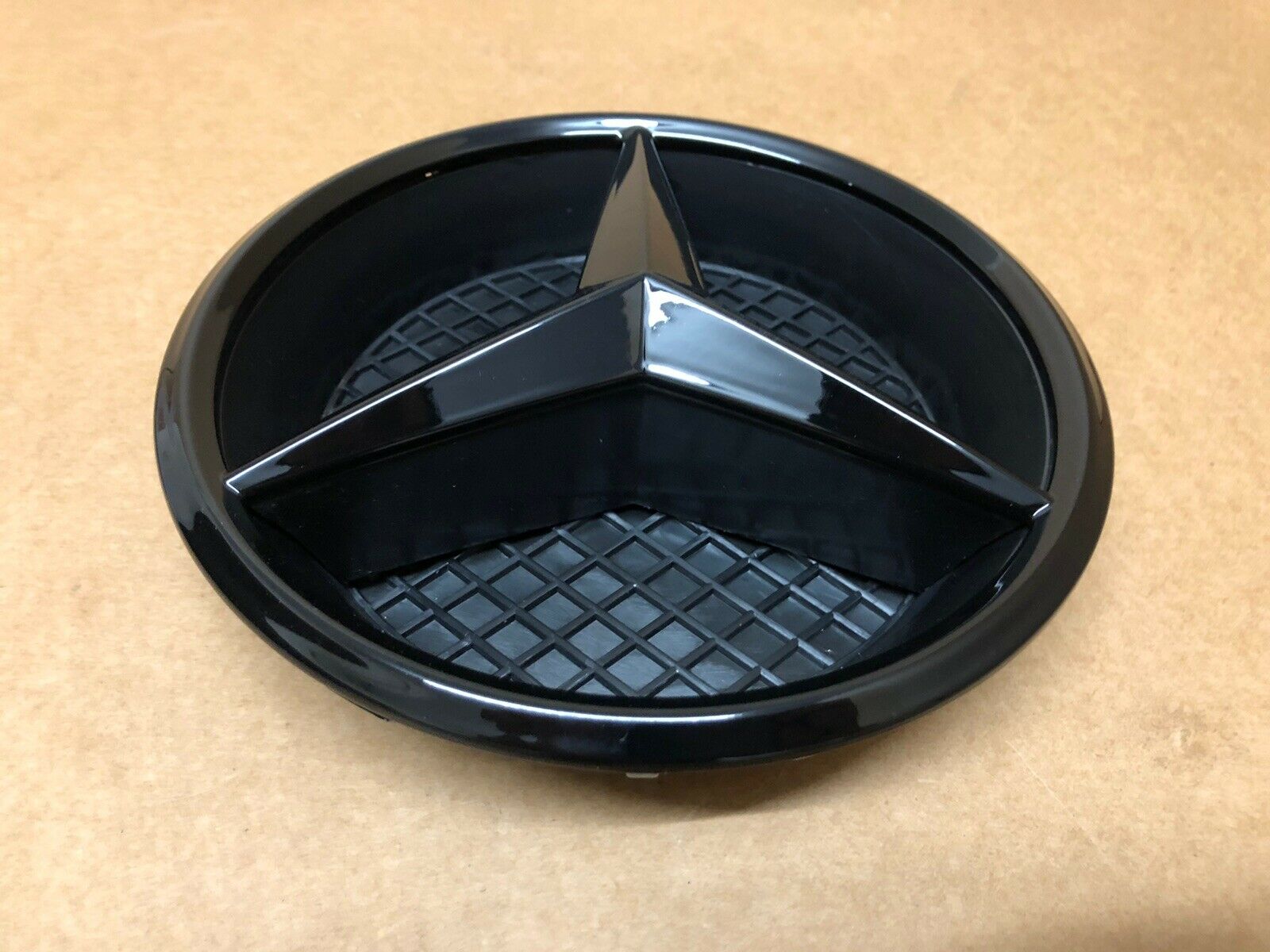 A sleek black Mercedes emblem badge for 2016+ Benz E-Class W213 front grille displayed on a table.