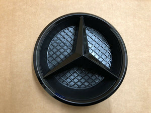 Black plastic Mercedes emblem for 2016+ Benz E-Class W213 front grille, displayed on a table.