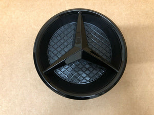 Black Mercedes emblem with base for 2016+ Benz E-Class W213 front grille on a table.
